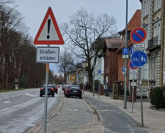 Straßenschäden Schild zwischen Straße und Radweg