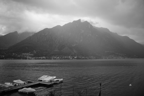 Schwarz-weiß Foto vom westlichen Ende des Lago Lugano. Blick auf den gegenüberliegenden Berg, weiße Boote im Vordergrund