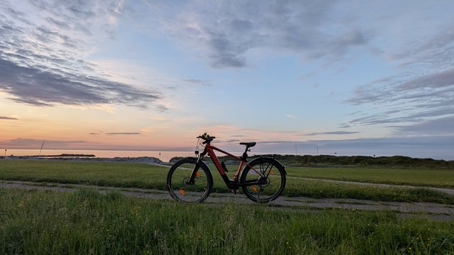 Ein rotes Raleigh Dundee Mountainbike steht auf dem Landesschutzdeich, dahinter das Meer und der Abendhimmel. 